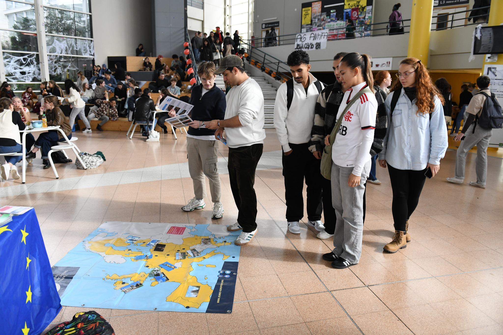 un groupe d'étudiantes et d'étudiants regardent une carte de l'Europe posée au sol dans le hall du bâtiment L sur le campus Villejean