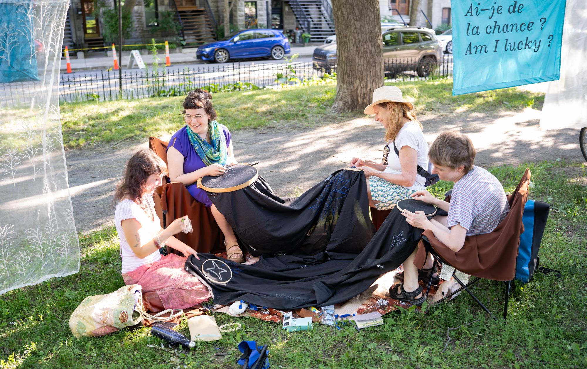 4 femmes brodent des étoiles sur un même tissu dans un parc