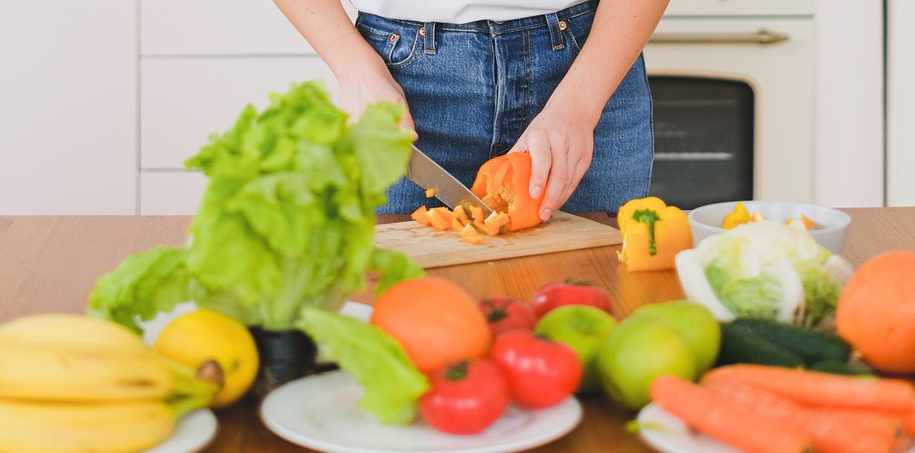 Mains d'une jeune femme en t-shirt blanc tranchant des légumes dans une cuisine moderne, se concentrant sur une alimentation saine.