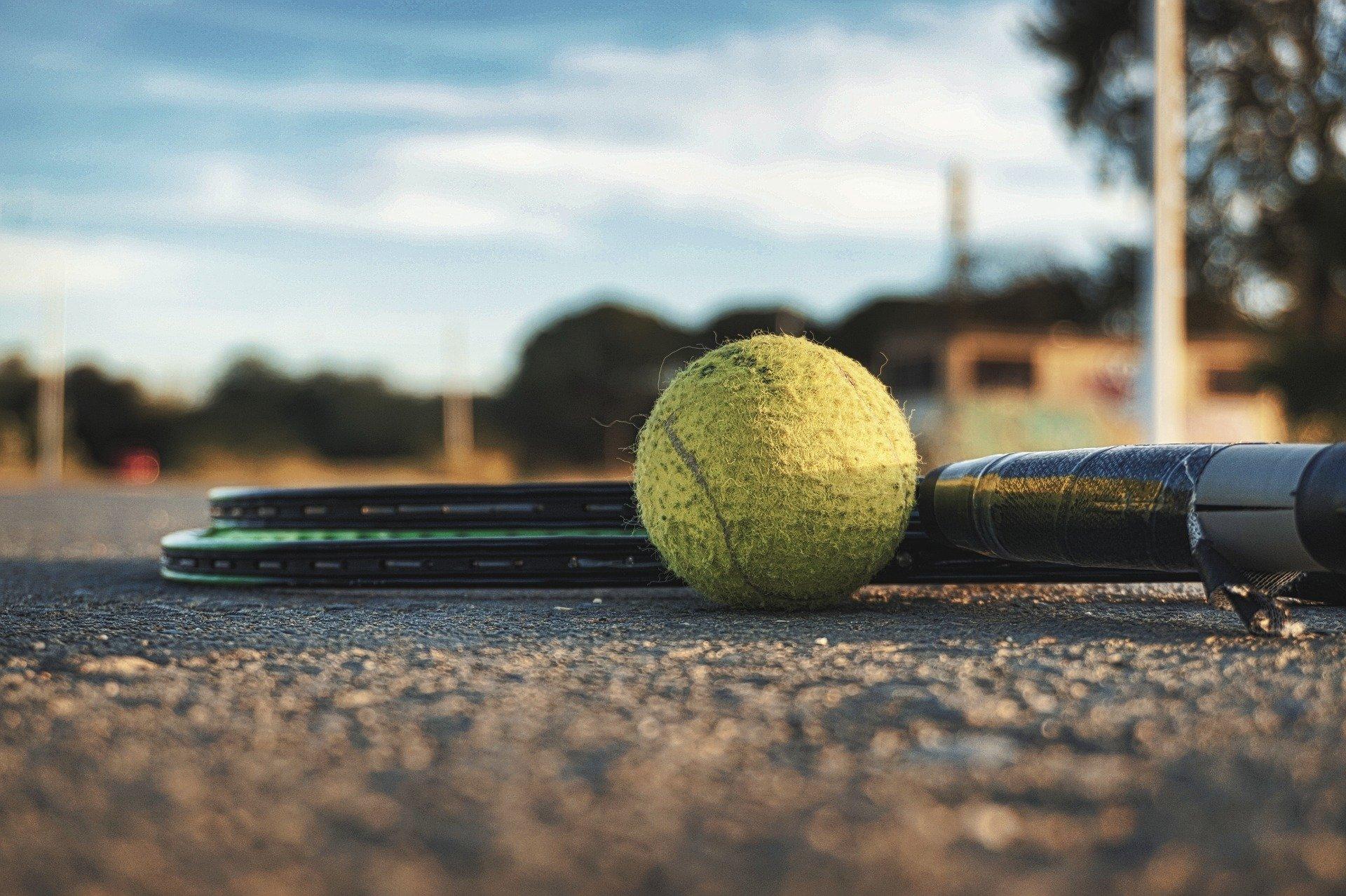 Photo d'une balle de tennis au sol à côté de 2 raquettes