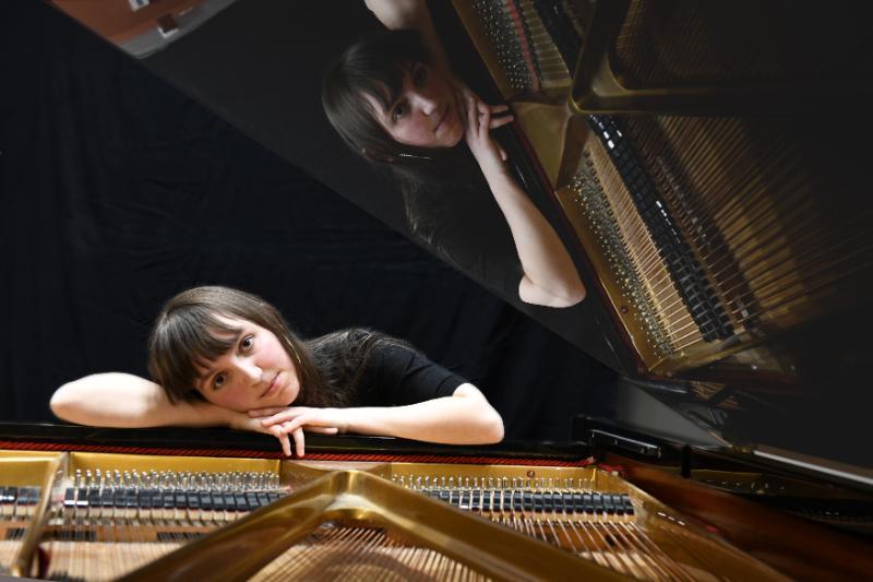 Piano WonderDream (Jola Verin) appuyée sur un piano à queue ouvert, avec son reflet visible dans le couvercle.