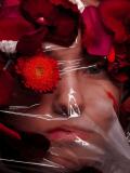 photo d'une femme dont on voit le visga derrière un plastique transparent, avec des fleurs et des pétales devant. La photo illustre la claustrophobie, qui est le nom de la photo