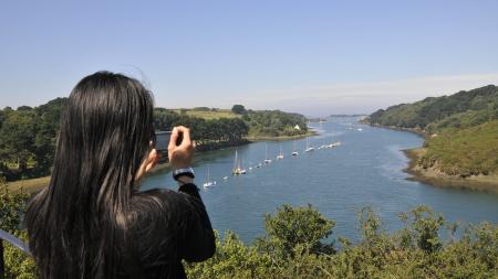 une femme de dos prend une photo avec son téléphone du paysage de l'Aber Wrac'h dans le Nord Finistère en Bretagne