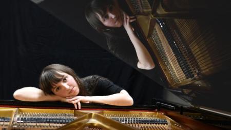 Piano WonderDream (Jola Verin) appuyée sur un piano à queue ouvert, avec son reflet visible dans le couvercle.