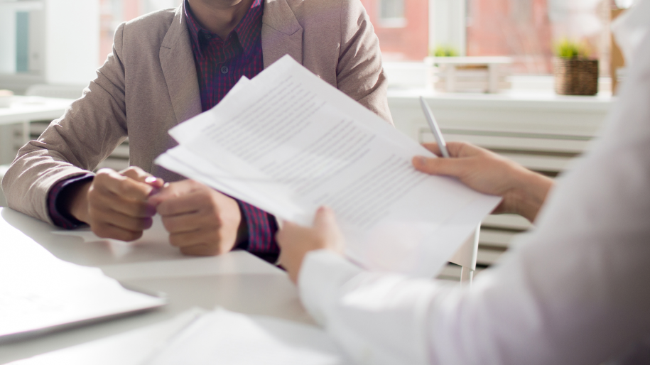 Entretien d'embauche entre deux personnes échangeant des documents dans un bureau lumineux.