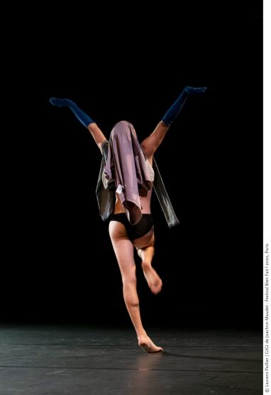 Joachim Maudet sur scène, de dos, dansant en slip et portant un vêtement sur sa tête et des chausettes bleu foncées sur ses deux avant-bras