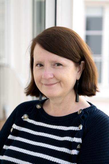 Portrait de Christelle Taraud, elle porte un carré, des boucles d'oreilles noires et un haut noir avec des rayures blanches.