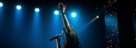 Photo d'une personne avec son micro, le bras levé et les projecteurs bleus en arrière-plan