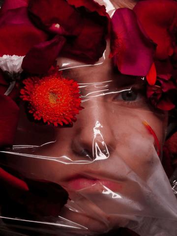 photo d'une femme dont on voit le visga derrière un plastique transparent, avec des fleurs et des pétales devant. La photo illustre la claustrophobie, qui est le nom de la photo