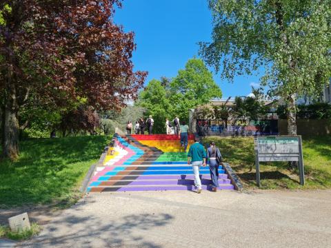 Des personnes montent les escaliers peint au couleurs du drapeau LGBTQIA+ de l'Université Rennes 2, sur le mûr en haut des marches on lit le message tagué "Nos fiertés plus fortes que leur haine"
