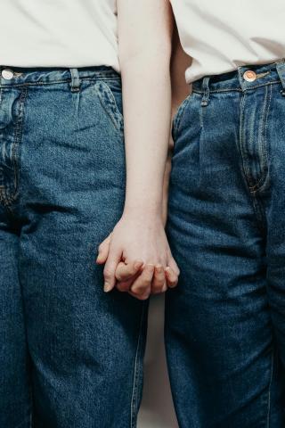 Photo en plan rapproché où on y voit deux femmes en jeans se tenir la main 
