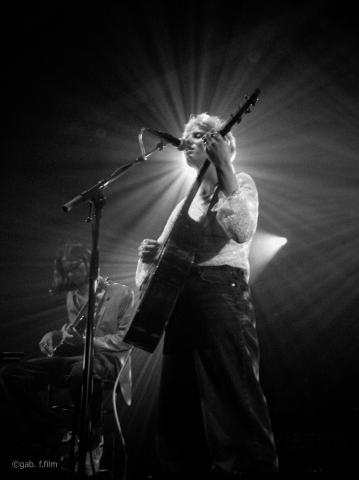 Kat White en concert live sur scène, en train de chanter une guitare à la main