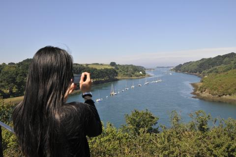 une femme de dos prend une photo avec son téléphone du paysage de l'Aber Wrac'h dans le Nord Finistère en Bretagne