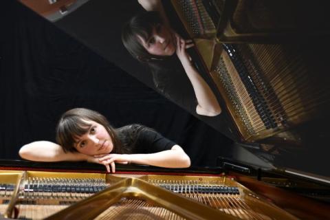 Piano WonderDream (Jola Verin) appuyée sur un piano à queue ouvert, avec son reflet visible dans le couvercle.